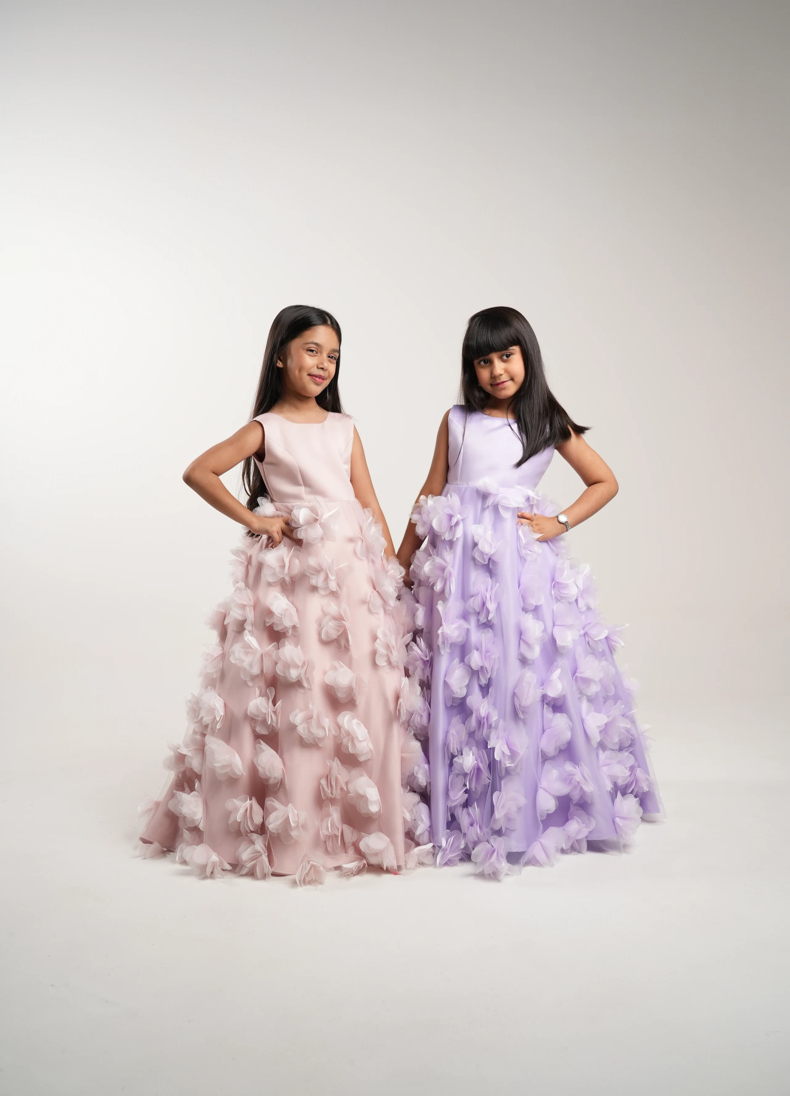 Two young girls in pink and lilac floral gowns on a pale studio backdrop.