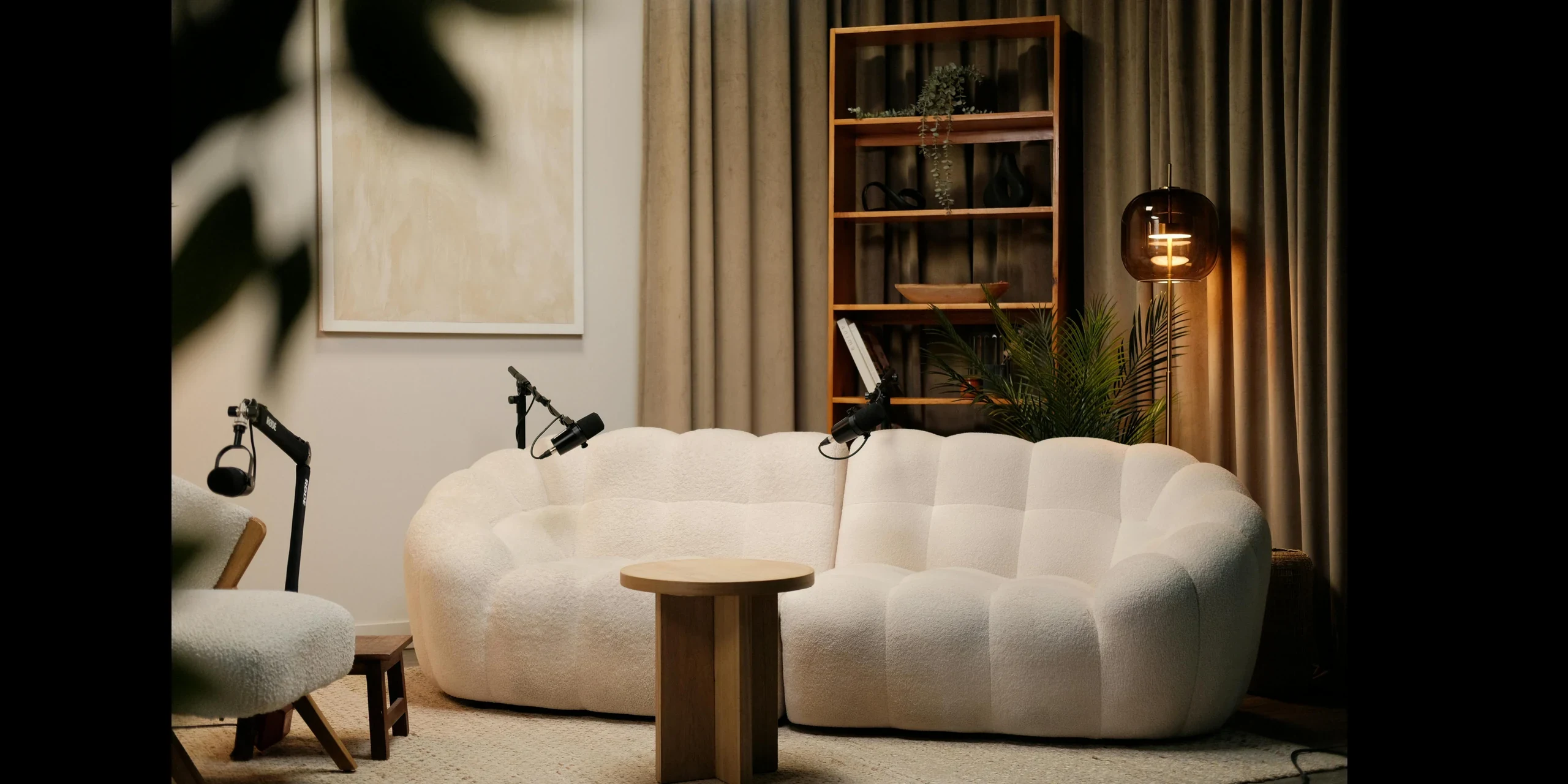 The podcast studio: a curved bouclé sofa between pleated curtains and shelving, with boom-mounted microphones either side.